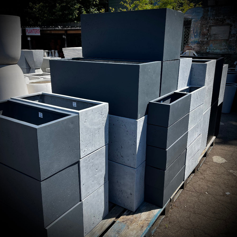 Stack of gray lightweightconcrete planters on a pallets outdoors.